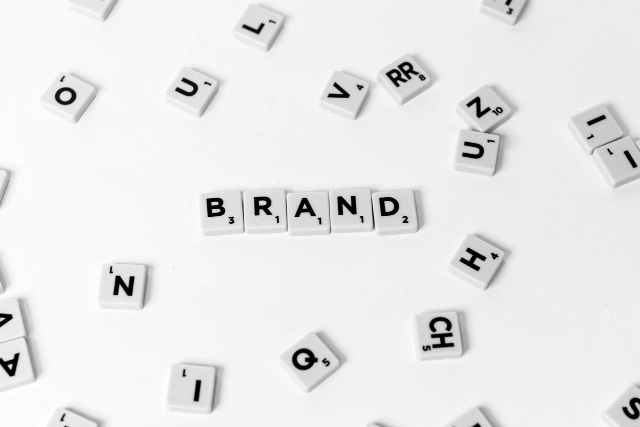 A flat-lay arrangement of scattered letter tiles spelling out BRAND against a white backdrop.